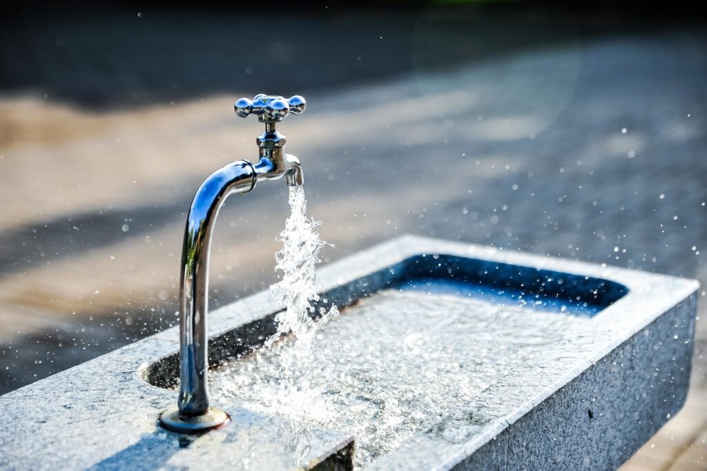 Grifo metálico vertiendo agua fresca en una fuente, imagen para explicar cómo beber agua correctamente.